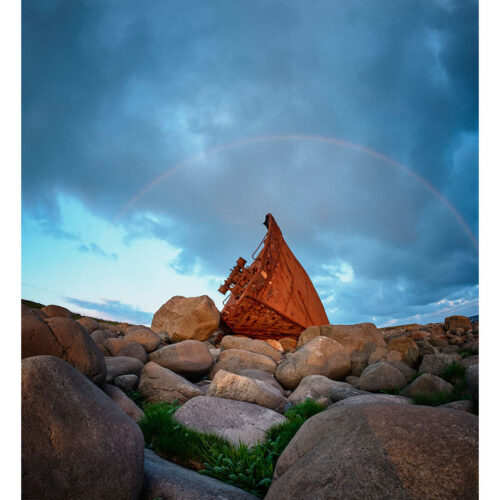 The front part of the freezer ship "Nortdfrost" that straded in 1967 bathe in sunset at Madland Hamn with a rainbow above at Hå, Jæren, Rogaland, Norway.